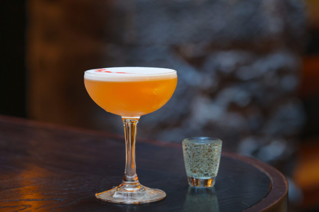 Pornstar martini cocktail served in a coupe glass, garnished with half a passionfruit and accompanied by a small shot glass of prosecco.